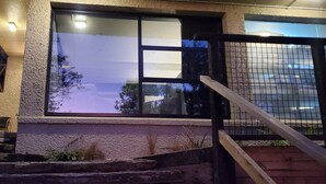 Un edifici amb una finestra gran que reflecteix arbres i un cel serè. Hi ha una escala de fusta que mena a l'entrada.