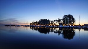 Un port de plaisance au crépuscule, avec des eaux calmes qui reflètent les bateaux et les arbres.