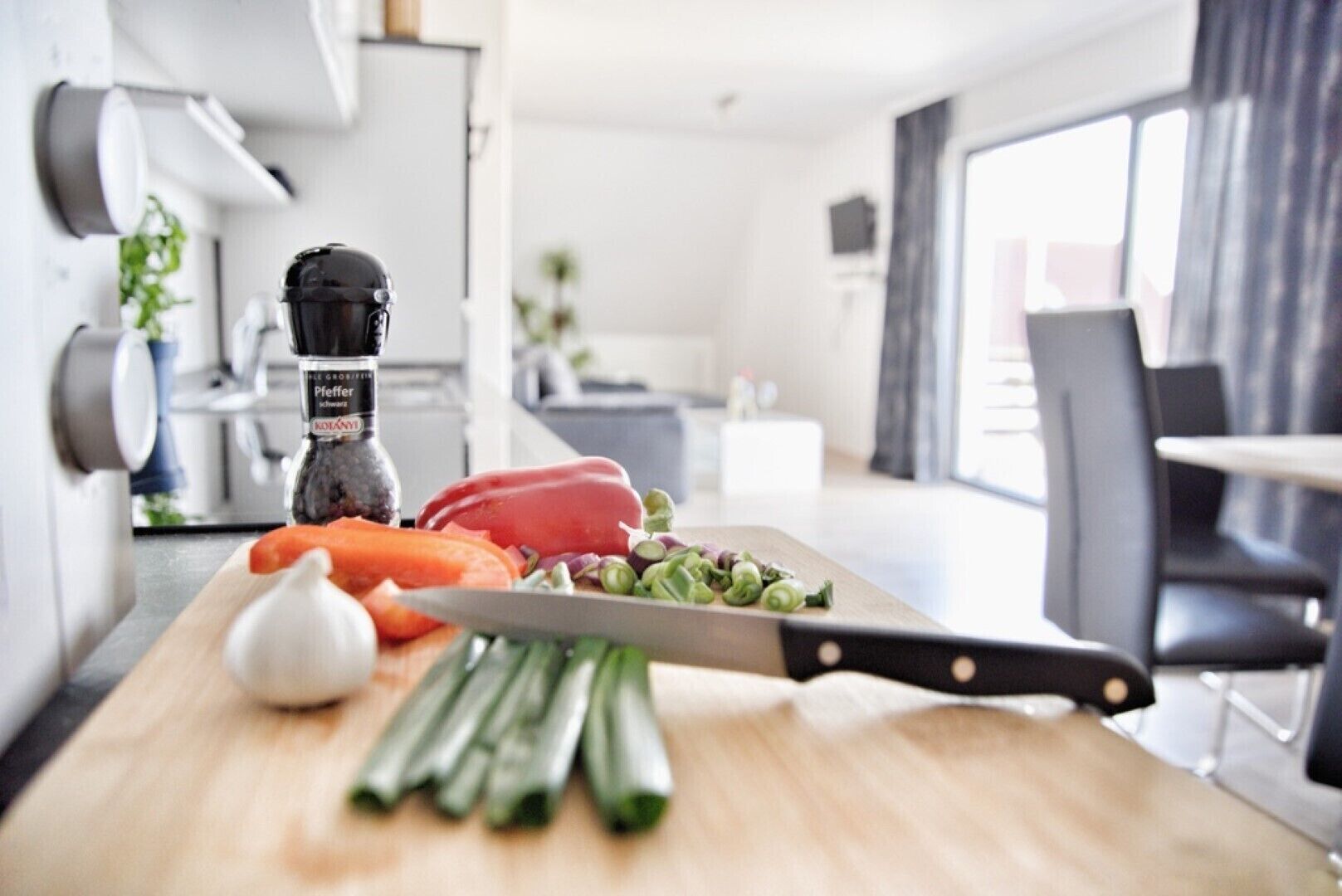 Una cocina moderna con encimera de madera, tabla de cortar con verduras, un cuchillo y un molinillo de pimienta.