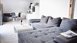 Un salon moderne avec un canapé d’angle gris, une table basse blanche et un coin repas à l’arrière-plan.