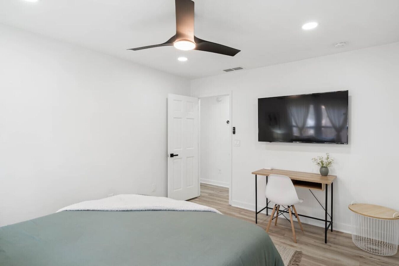 Un dormitorio moderno con cama, escritorio, silla, televisor y ventilador de techo.