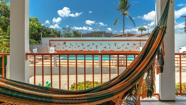 Un hamac sur un balcon donnant sur une piscine, avec un mur carrelé et des palmiers en arrière-plan.