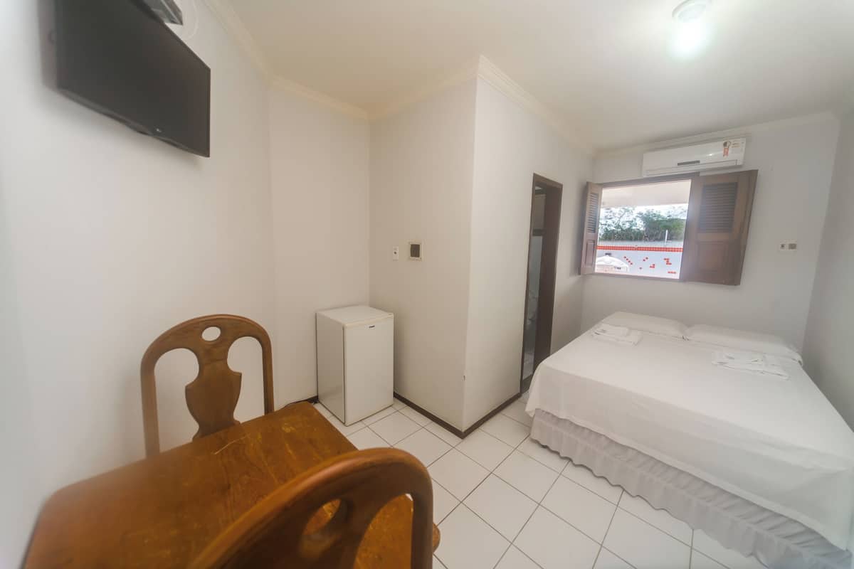 Une chambre à coucher comprenant un lit, une petite table, une chaise, une armoire blanche et un téléviseur fixé au mur.