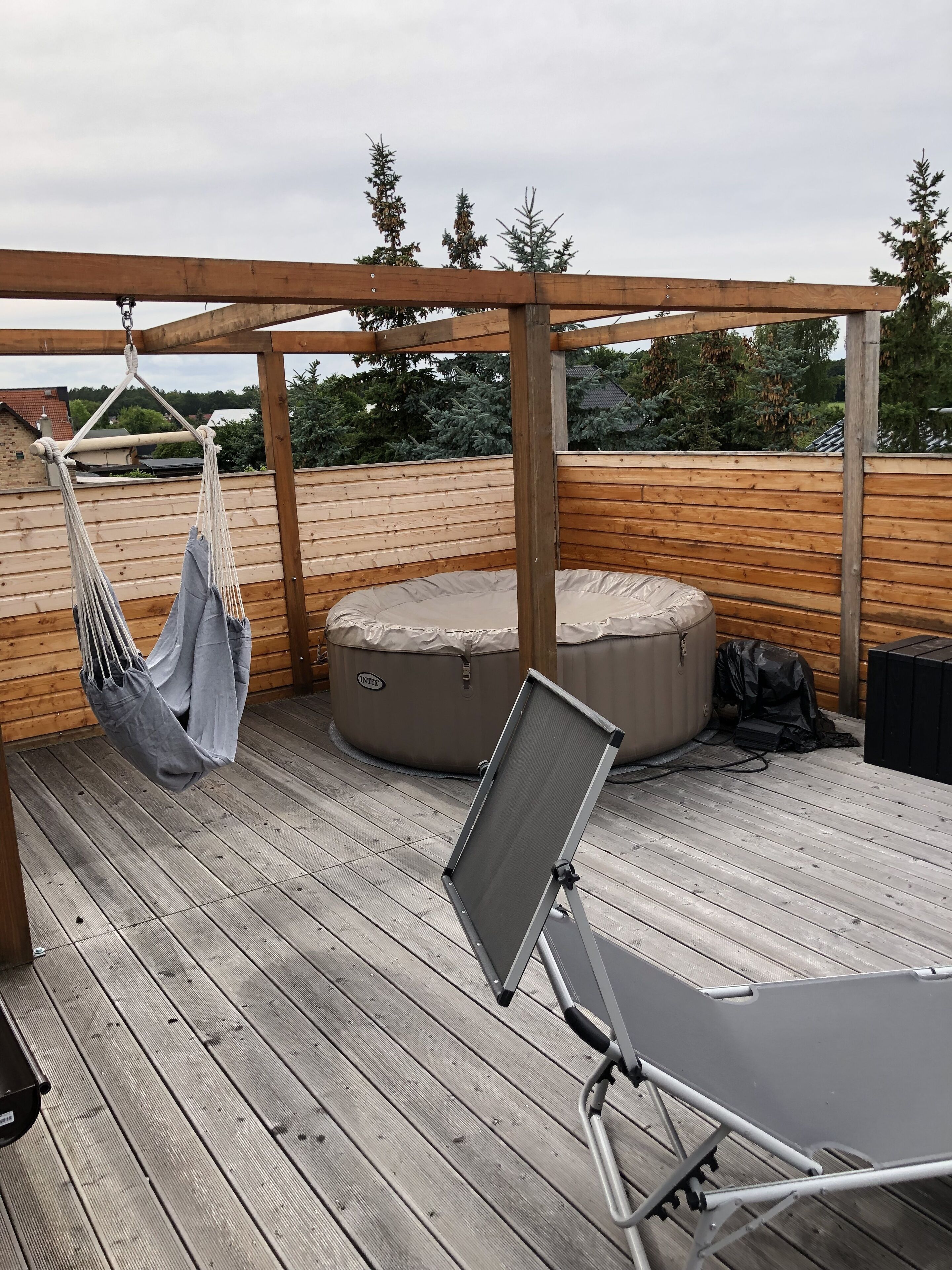 Une terrasse en bois avec un hamac, une chaise pliante et un espace salon circulaire.