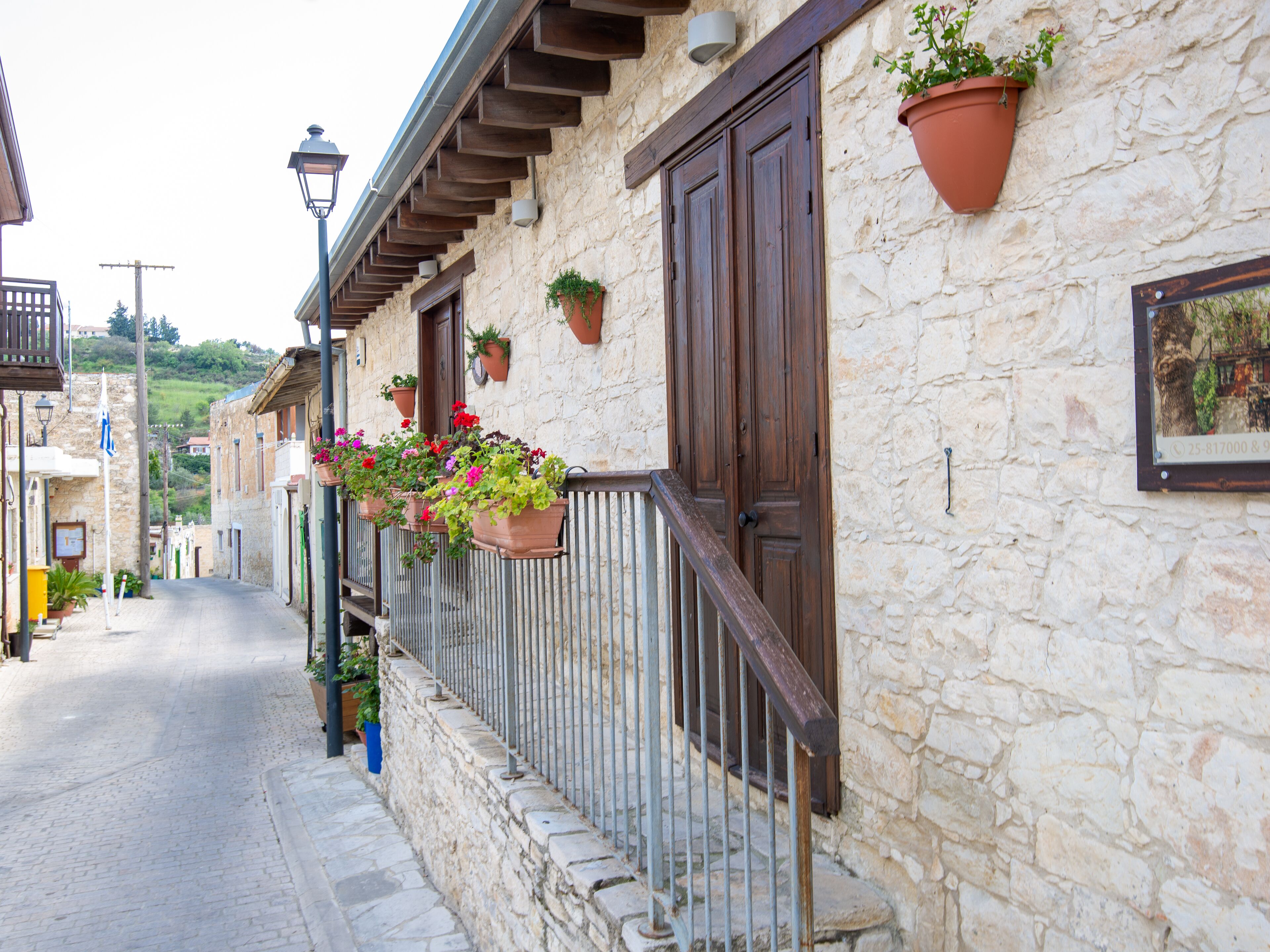 A stone building with wooden doors and windows, potted plants on the balcony, and a cobblestone street.