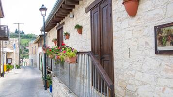 A stone building with wooden doors and windows, potted plants on the balcony, and a cobblestone street.