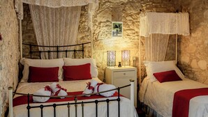 Ein Zimmer mit Steinwand, einem Bett mit roten Kissen, einem Nachttisch mit Lampe und einem kleinen Tisch mit Handtüchern.