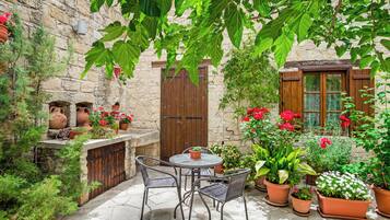Une cour dallée, avec une table et des chaises, entourée de plantes et de fleurs en pot.
