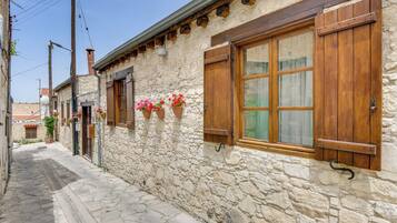 A narrow stone building with wooden shutters and flower boxes.