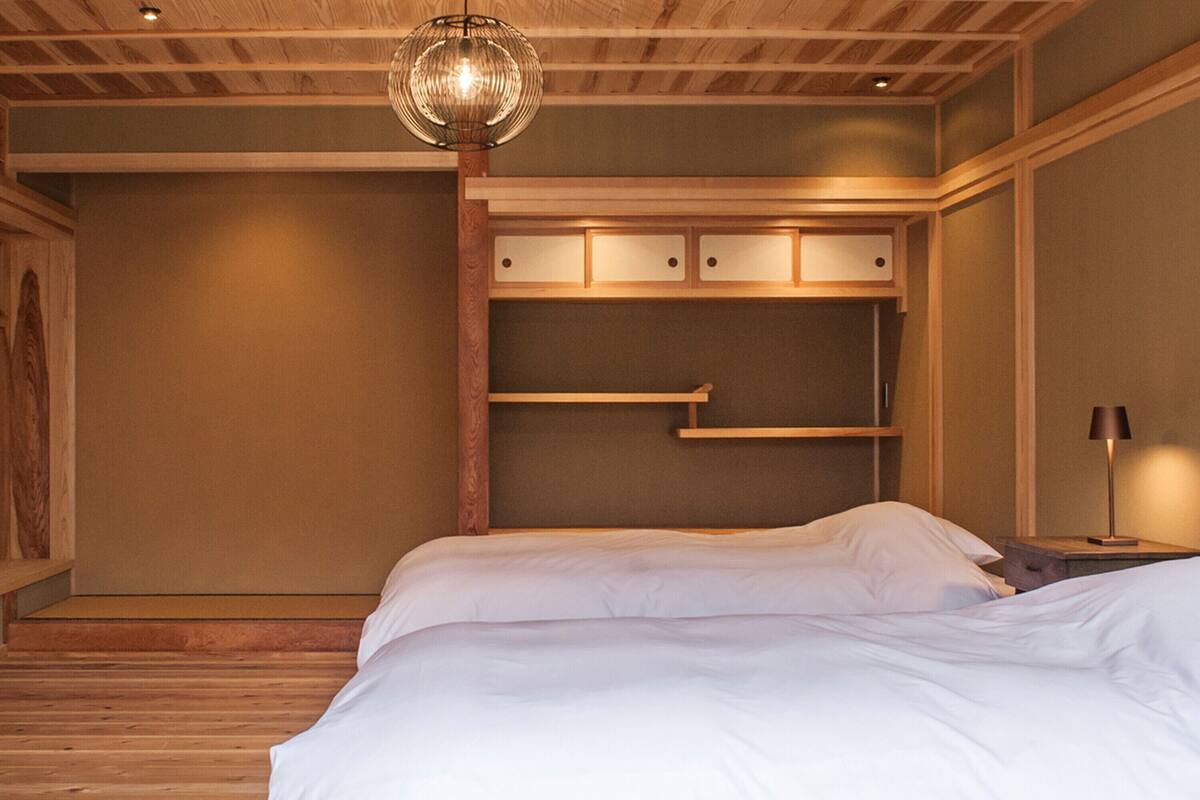 A bedroom with a wooden ceiling, a bed with white bedding, a hanging light fixture, and built-in shelves.