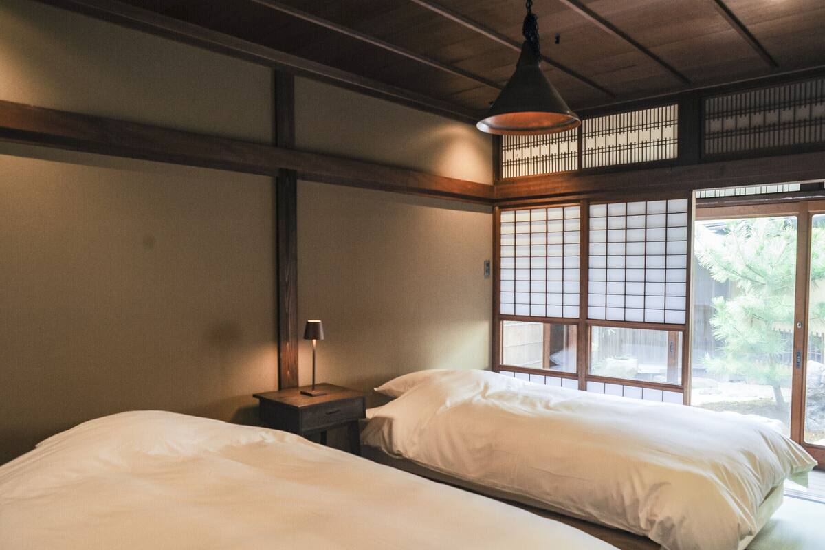 A traditional Japanese room with two beds, a wooden ceiling, and a sliding shoji screen window.