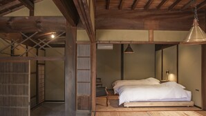 A traditional Japanese-style room with a wooden floor, a bed with white bedding, a hanging lamp, and a sliding door. - Nipponia Izumo Taisha Shrine Town (Izumo)