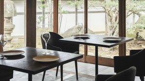 A dining area with a table set for two, a stone lantern, and a view of a traditional garden through large windows. - Nipponia Izumo Taisha Shrine Town (Izumo)