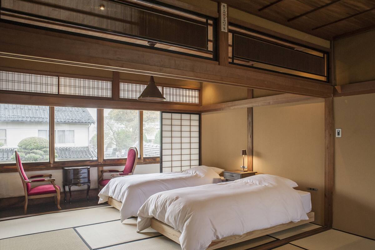 A traditional Japanese-style room with tatami flooring, two beds, a desk, and a chair.