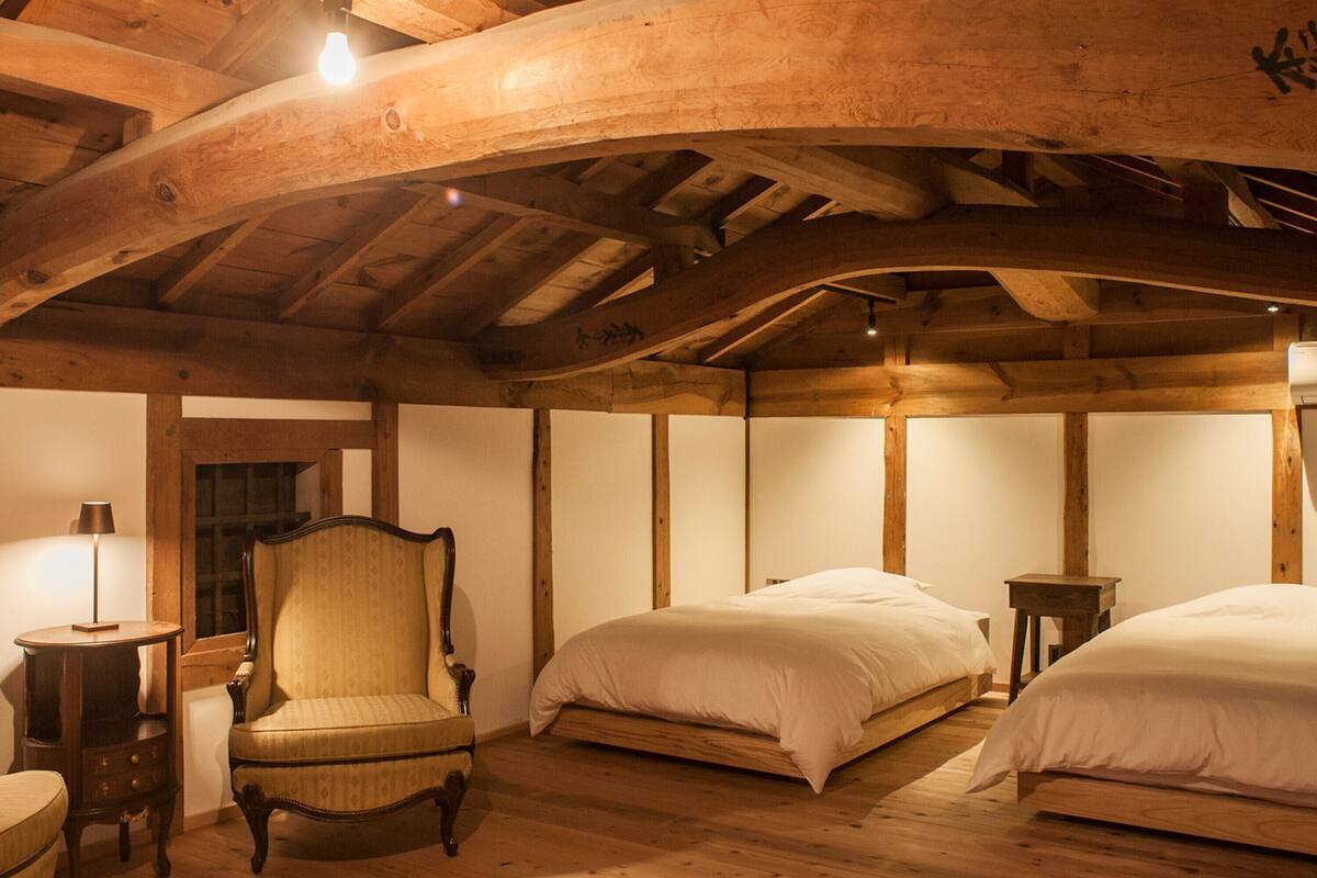 A room with wooden beams, a chair, two beds, and a lamp.