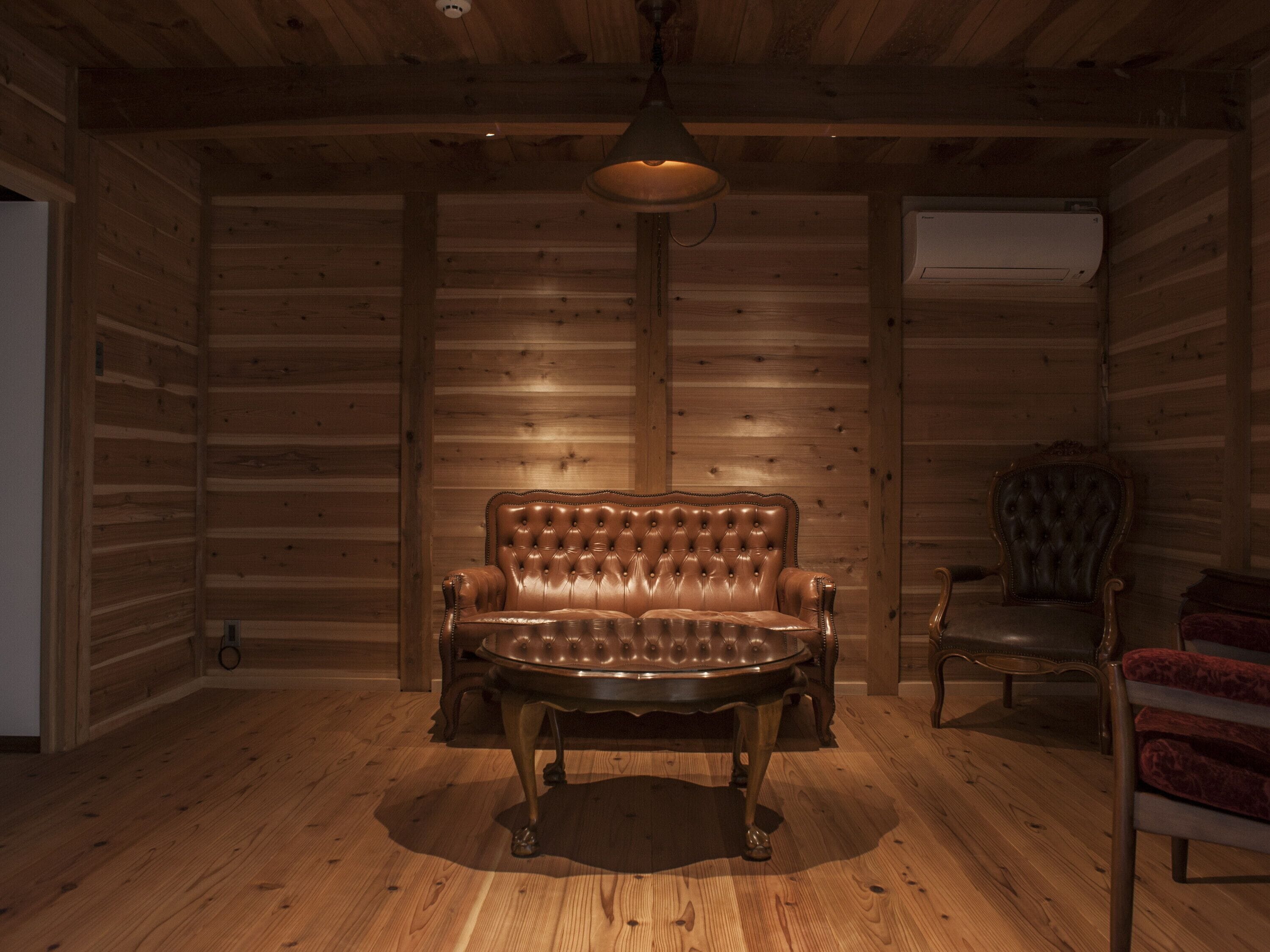 Interior de una cabaña de troncos con sofá de cuero, techo de madera y lámpara colgante.