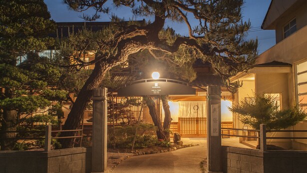 A traditional Japanese building entrance with a large tree in the center, a signboard, and a stone pathway leading to the entrance. - Nipponia Izumo Taisha Shrine Town (Izumo)