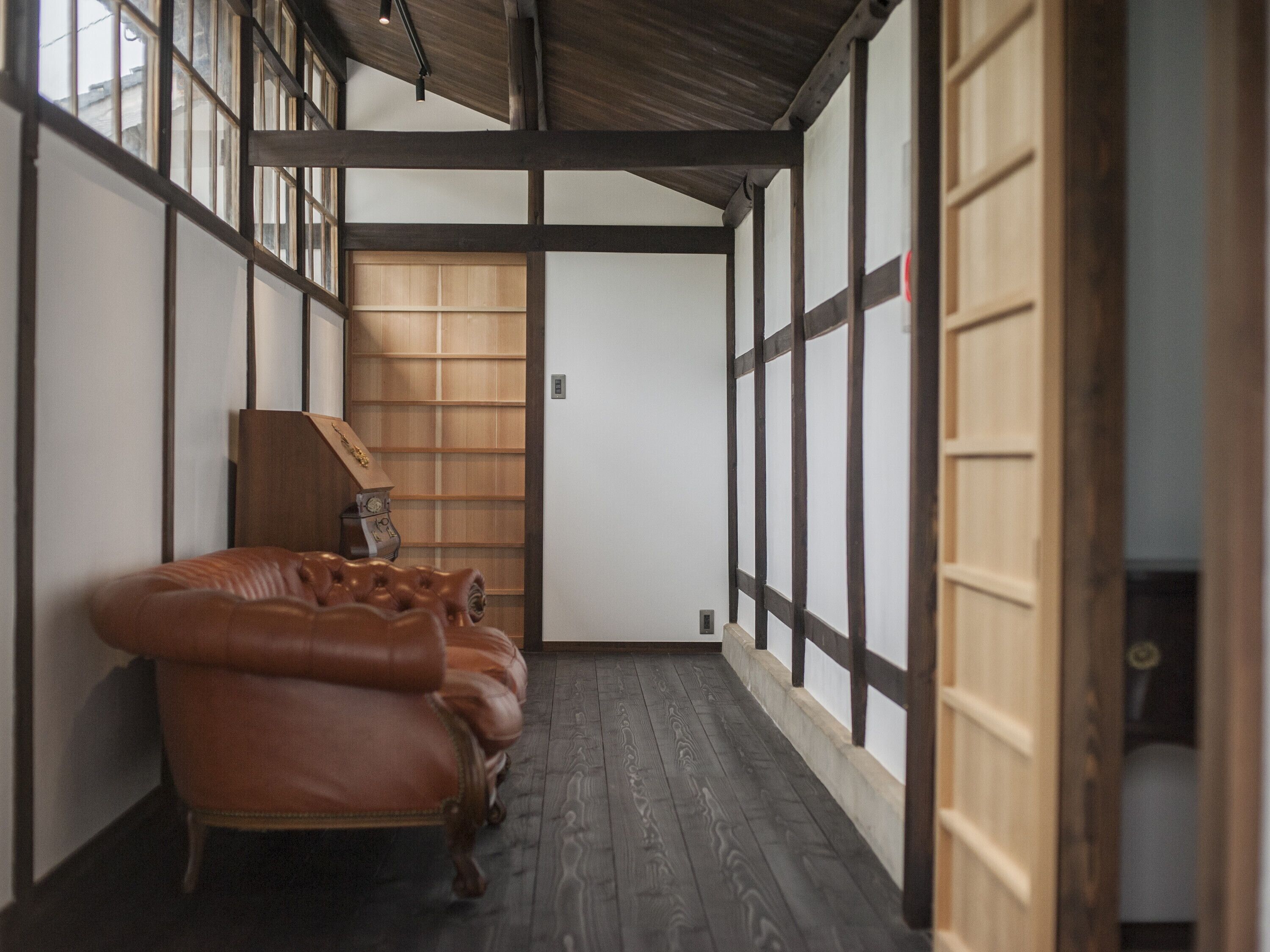 A traditional Japanese room with tatami flooring, a brown leather sofa, and wooden sliding doors.