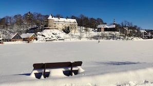 A snow-covered landscape with a large building on a hill, a smaller structure with a steeple, and a bench in the foreground. - The Perfect House to Stay for Holidays (Oberharz am Brocken)