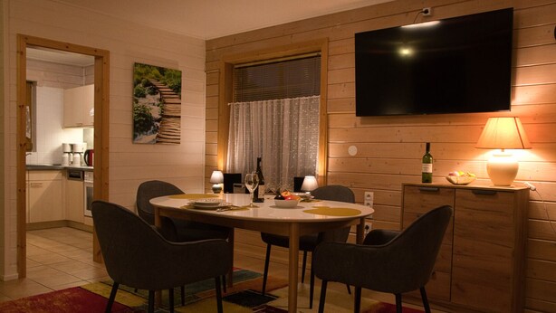 A dining area with a round table, chairs, a TV mounted on the wall, a lamp, and a bottle of wine. - The Perfect House to Stay for Holidays (Oberharz am Brocken)