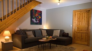 A living room with a dark-colored sofa, a coffee table, a lamp, a painting, and a wooden door. - The Perfect House to Stay for Holidays (Oberharz am Brocken)