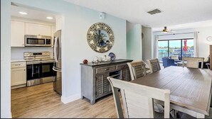 A modern kitchen with stainless steel appliances, a dining area with a wooden table and chairs, and a decorative wall clock. - Beautiful waterfront view property. Only 5 minutes from the beaches! (Clearwater)