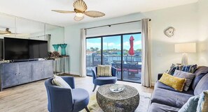 Ein Wohnzimmer mit einer Couch, Sesseln, einem Couchtisch, einem Fernseher und einem Balkon mit Blick.