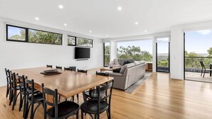 A spacious living area with a wooden dining table, black chairs, a grey sofa, and a flat-screen TV mounted on the wall. - Ultimate Coastal Haven , Private Pool & Sun Aspect (Anglesea)