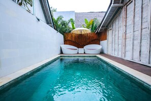 A swimming pool with two white lounge chairs and a wooden fence with plants.