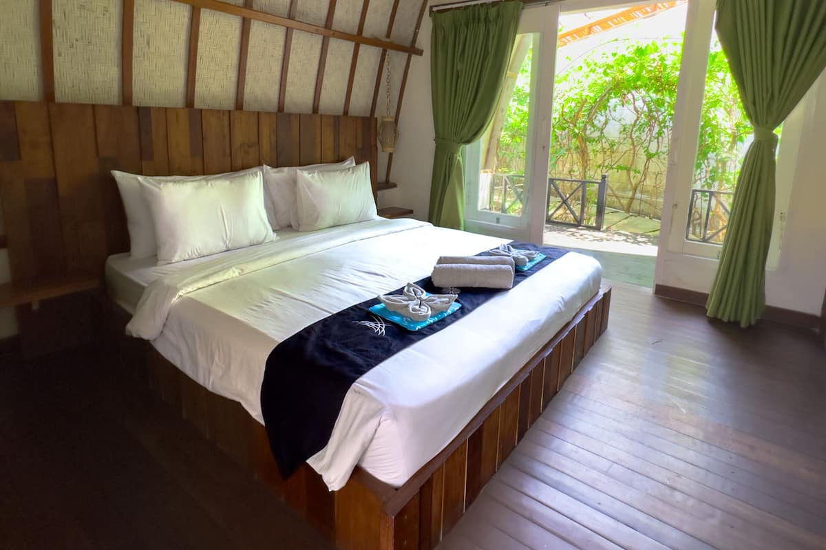 A spacious bedroom with a large bed, wooden headboard, and a view of greenery through the windows.