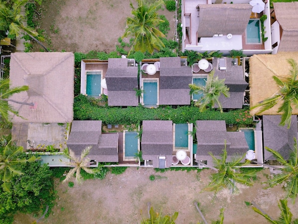 An aerial view of a resort with multiple bungalow-style accommodations, each with a private pool and surrounded by lush greenery and palm trees.