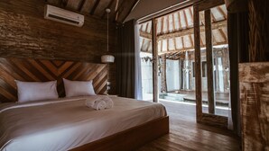 A wooden-paneled bedroom with a large bed, a ceiling fan, and a view through a glass door to an outdoor area. - CAMILLA RESORT (Gili Air)