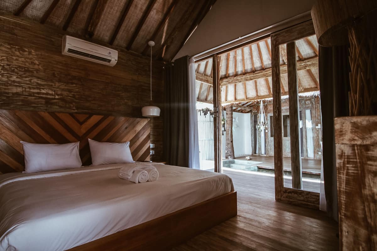 A wooden-paneled bedroom with a large bed, a ceiling fan, and a view through a glass door to an outdoor area.