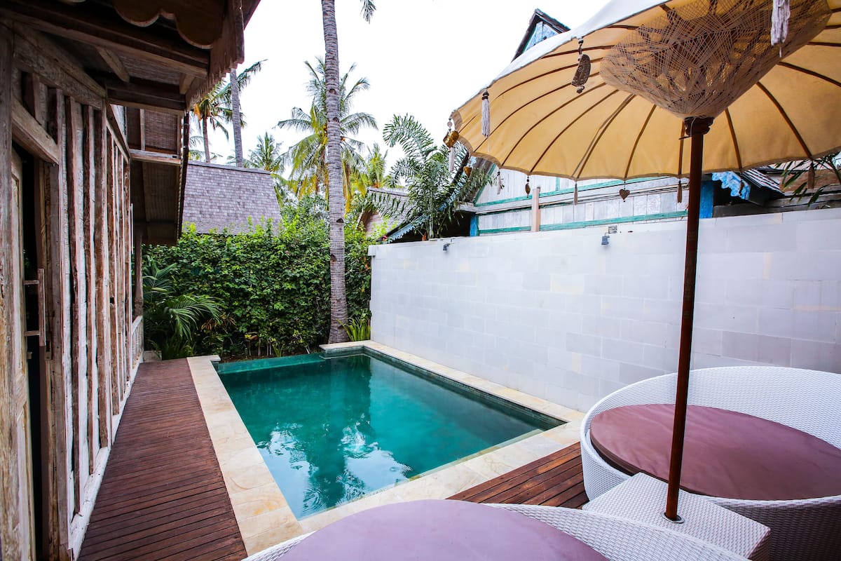 A pool area with a wooden deck, a white tiled wall, and a wicker chair with a cushion.