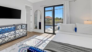 A modern hotel room with a large bed, a TV, a balcony with a pool view, and a decorative metal partition.