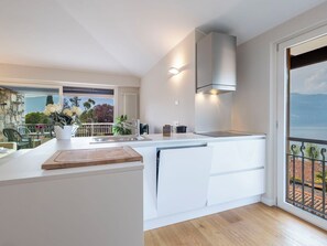 A modern kitchen with a built-in oven, a sink, and a window overlooking a balcony with outdoor furniture.