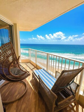 A balcony with wicker furniture, a striped table, and a view of the ocean.