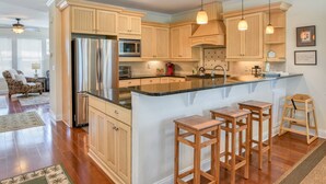 A spacious kitchen with wooden cabinets, a stainless steel refrigerator, a microwave, and a large island with bar stools. - Large Family Home, 1 minute Walk to Beach, Private Yard, Heated Pool, Elevator, $300 in Free Tickets (St. Augustine)