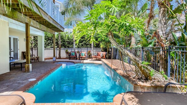 A swimming pool with a wooden deck, surrounded by a fence and lush greenery. - Large Family Home, 1 minute Walk to Beach, Private Yard, Heated Pool, Elevator, $300 in Free Tickets (St. Augustine)