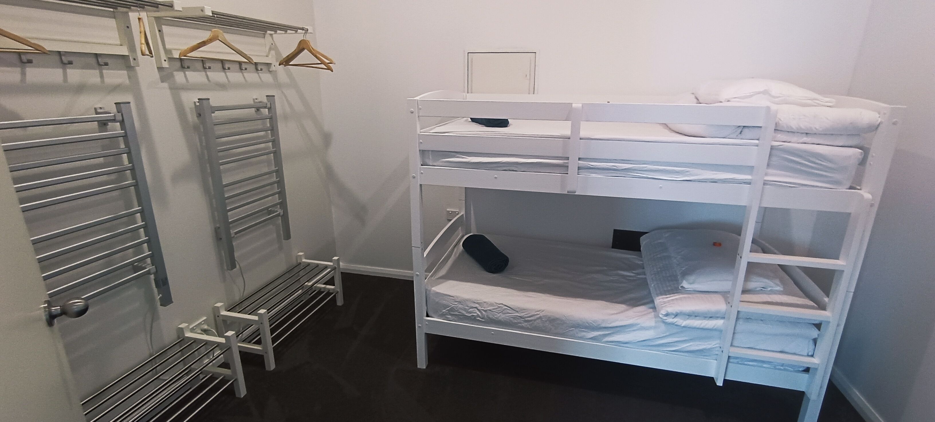 Habitación con literas, un estante metálico y un pequeño banco.