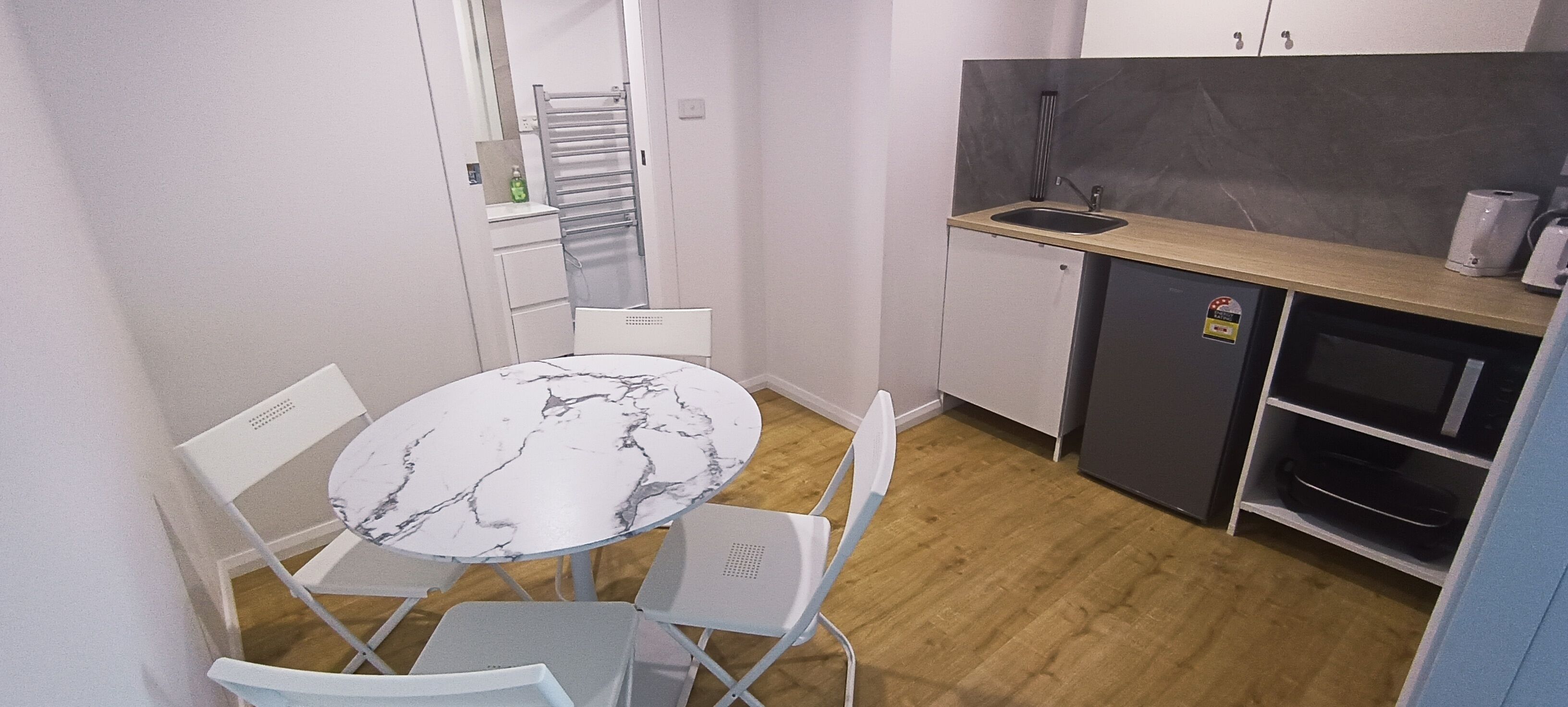 Een compacte keuken met een marmeren tafel en witte stoelen, een klein spoelgedeelte en een inbouwoven.
