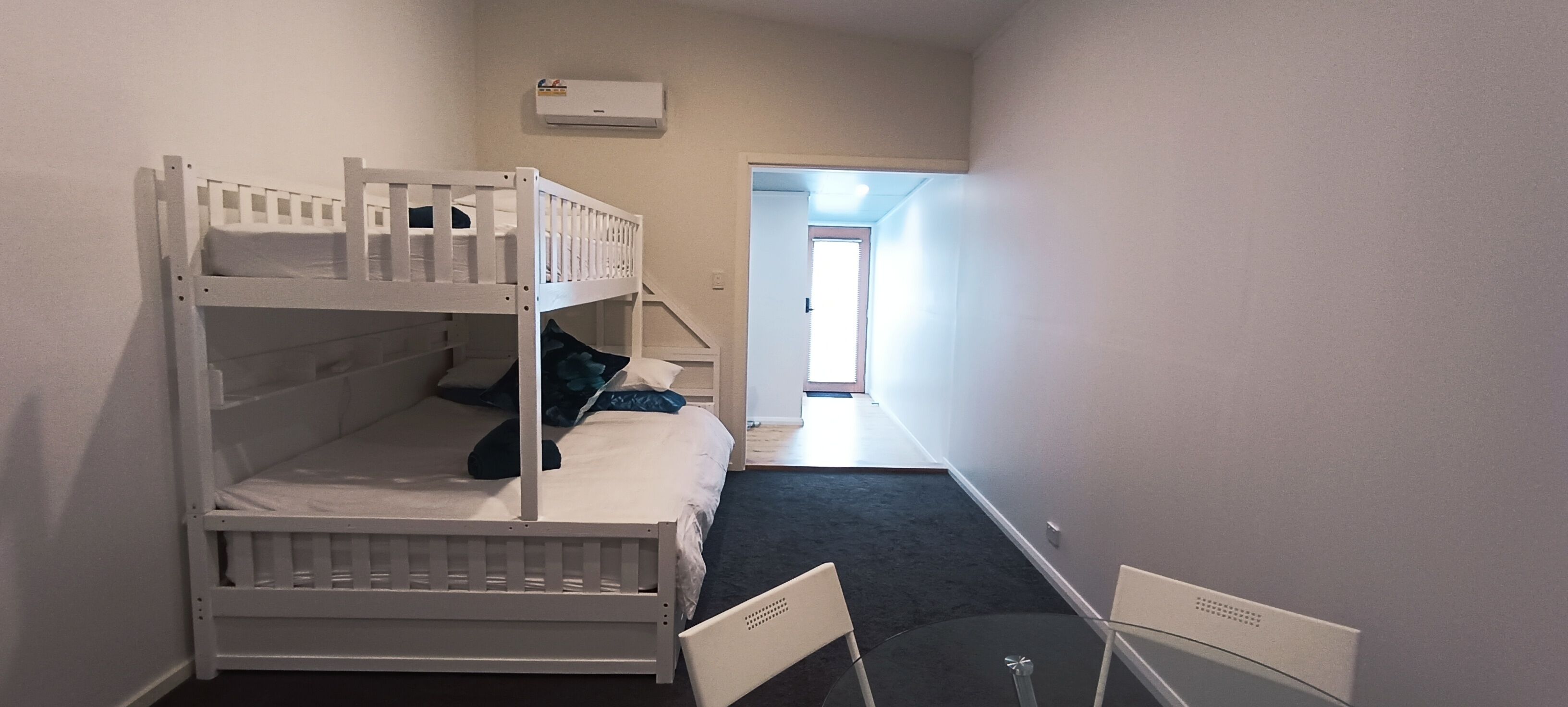 A bunk bed room with a small table and chairs, a window, and an air conditioning unit on the wall.