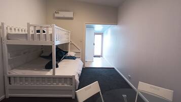 A bunk bed room with a small table and chairs, a window, and an air conditioning unit on the wall.