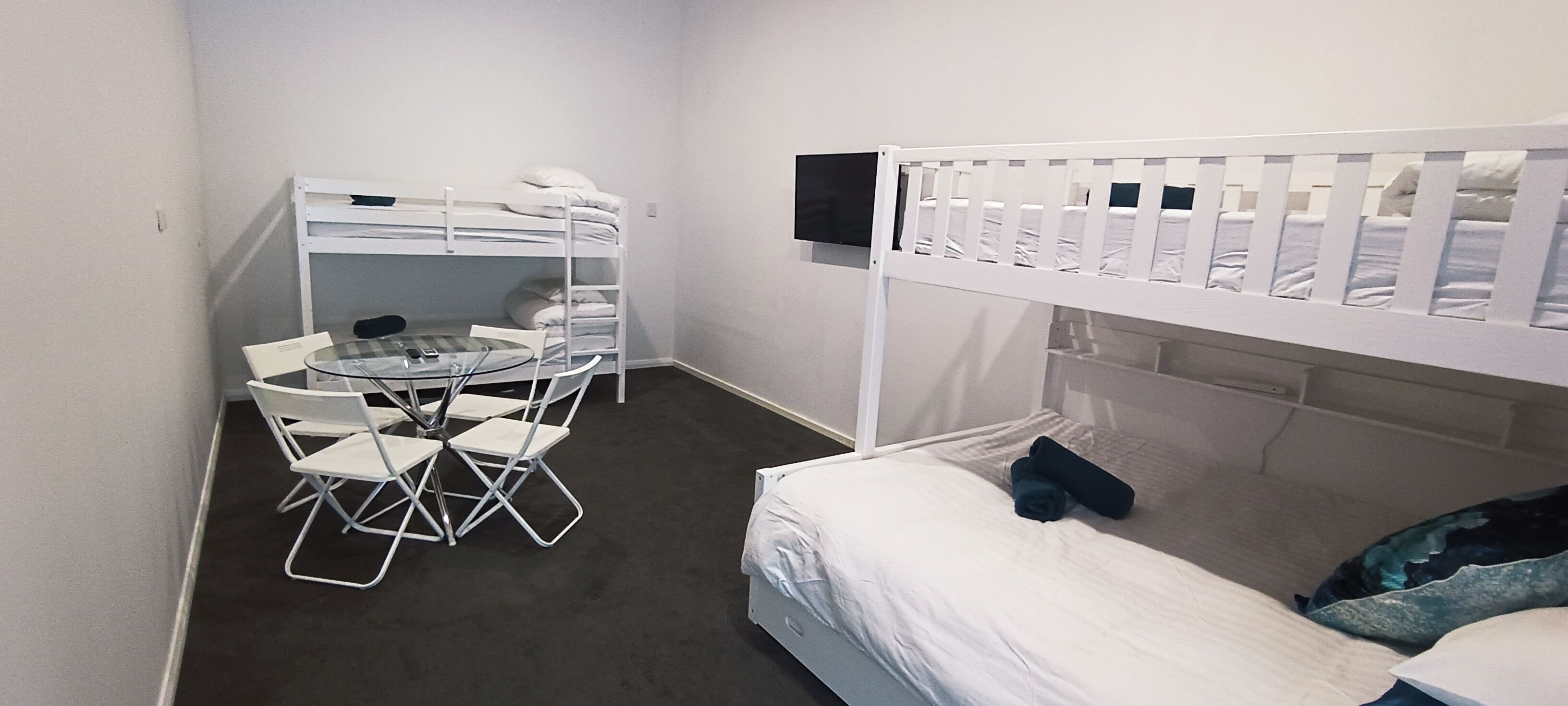 A bunk bed room with a desk and chairs, a TV mounted on the wall, and a window.