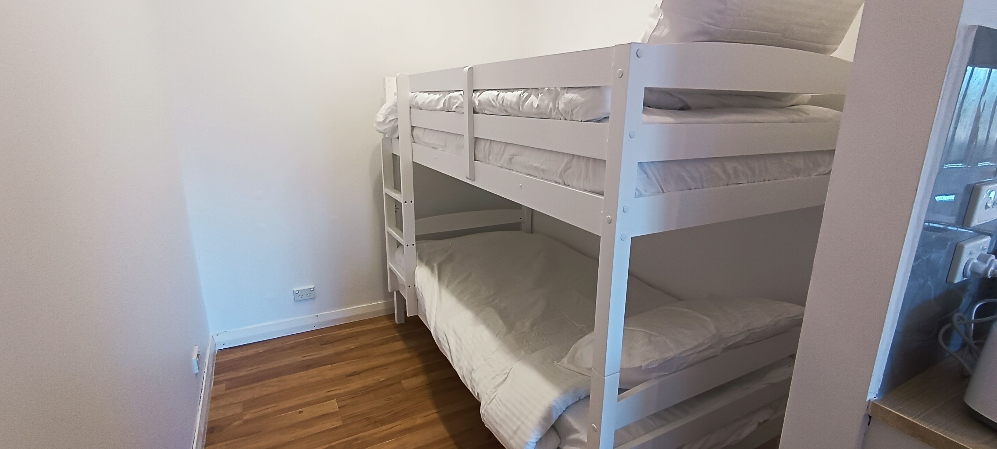 Une chambre avec un lit superposé, du linge de lit blanc et un plancher en bois.
