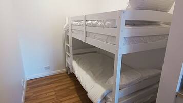 Dormitorio con literas, ropa de cama blanca y suelo de madera.