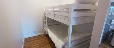 Une chambre avec un lit superposé, du linge de lit blanc et un plancher en bois.