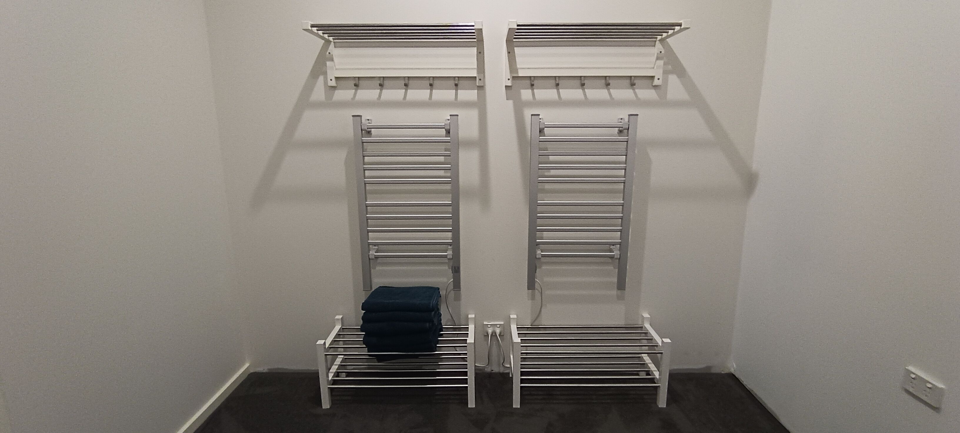 Ein Schrank mit zwei weißen Metallregalen und einer mittleren Kleiderstange, auf der gefaltete Kleidung liegt.