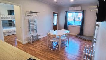 Ein kleines Zimmer mit Etagenbett, Tisch mit Stühlen, Heizkörper und Fenster mit Blick.