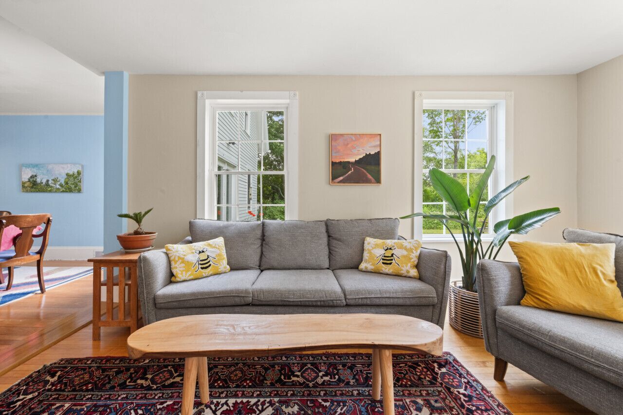 Een woonkamer met een grijze bank, twee gele kussens, een houten salontafel en een kamerkleed met dessin.